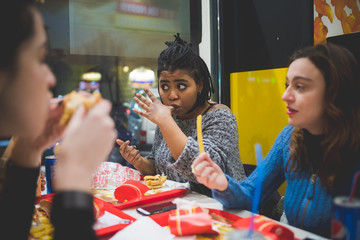 Obraz na płótnie Canvas multiracial girlfriends eating together in fast food