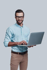 Looking for fresh ideas. Good looking young man carrying laptop and looking at camera while standing against grey background