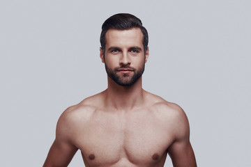 Young and handsome. Handsome young man looking at camera and smiling while standing against grey background