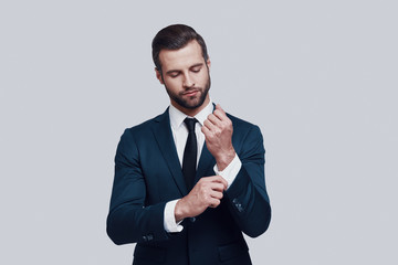 Confidence and charisma. Handsome young man adjusting his sleeve while standing against grey background