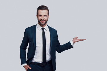 Take a look! Handsome young man pointing copy space and smiling while standing against grey background