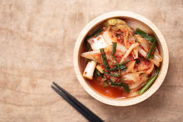 Kimchi cabbage in a bowl with chopsticks on wooden background, Korean food, top view