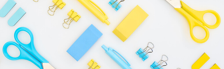 panoramic shot of yellow and blue erasers, pens, scissors and paper clips isolated on white