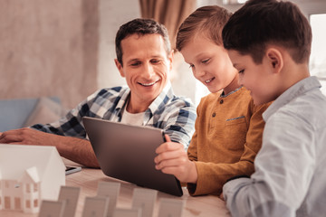 Fototapeta premium Two cute sons showing their photos to foster father on tablet
