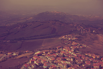 Beautiful landscape of mountains and rural town under blue fog sky from high view of San Marino city. Violet portrait