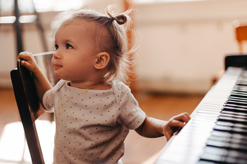 Cute little happy child girl playing piano in a light room. Selective focus, noise effect