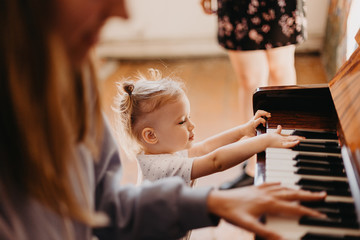 a portrait of a cute 2-year-old happy baby who has fun at the piano lesson. Little child girl playing piano in a light room. Selective focus, noise effect © Максим Галінский