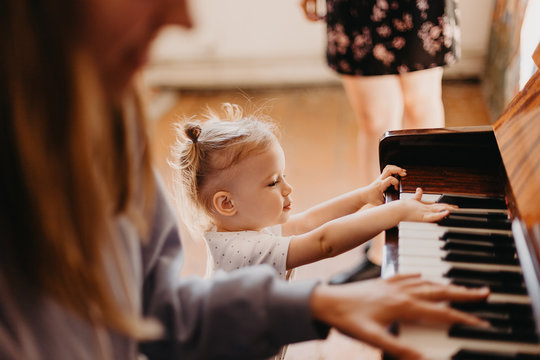 a portrait of a cute 2-year-old happy baby who has fun at the piano lesson. Little child girl playing piano in a light room. Selective focus, noise effect