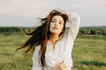 Portrait of beautiful carefree long hair girl in white clothes on field at sunset. Sensitivity to...