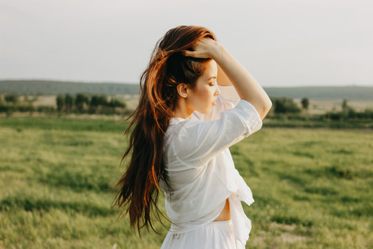 Portrait of beautiful carefree long hair girl in white clothes on field at sunset. Sensitivity to nature concept
