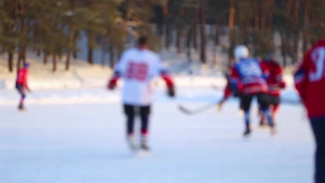 Defocused people playing hockey game on rink at frozen river outdoors on sunny frosty cold day. Real time full hd video footage.