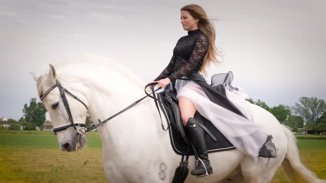 beautiful blonde girl with black dress rides a white horse in slow motion