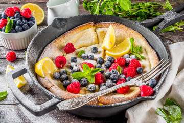 Sweet breakfast vegan dutch baby baked pancake with fruit and berries, wooden background copy space