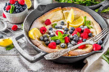 Sweet breakfast vegan dutch baby baked pancake with fruit and berries, wooden background copy space