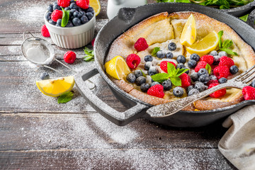 Sweet breakfast vegan dutch baby baked pancake with fruit and berries, wooden background copy space