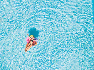 Beautiful young woman lay down enjoying and relaxing on an inflatable ice cream lilo in a blue clear swimming pool - holiday summer vacation at hotel resort concept for people having fun