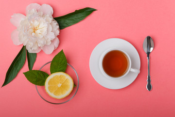 Obraz na płótnie Canvas A cup of tea, fresh lemon and white peony on a pink background.