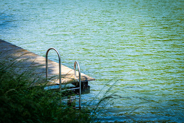 Old wooden pier with metal ladder into the lake