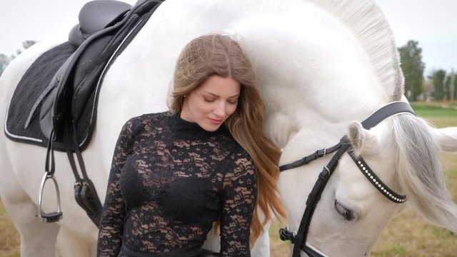 beautiful blonde girl with black dress strolls in the meadow with a white horse 