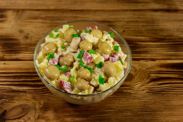 Potato salad with marinated mushrooms, sausage, onion and mayonnaise on wooden table