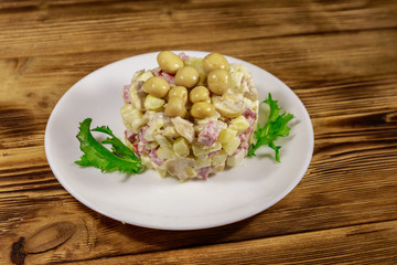 Potato salad with marinated mushrooms, sausage, onion and mayonnaise on wooden table