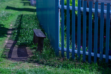 blue fence,bench and striped shade on a Sunny summer day