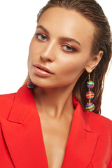 Closeup front shot of lady with tanned skin, wearing red blazer and long earrings with pendants in...