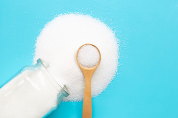 Wooden spoon with white granulated sugar on blue background.