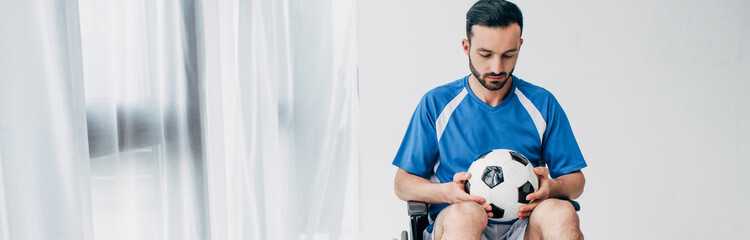 panoramic shot of man in football uniform sitting in Wheelchair and holding soccer ball