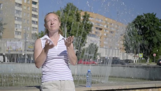 woman is exhausted from heat, waving her arms standing next to fountain.