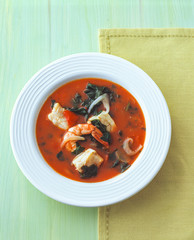 Tomato fish soup with shrimps and fish fillet and spinach on the plate