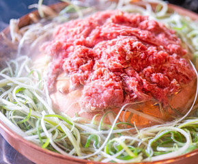 Beef barbecue bulgogi in Korean restaurant in Seoul, lifestyle fresh korean food cuisine on copper pan with sliced green onion, close up, copy space
