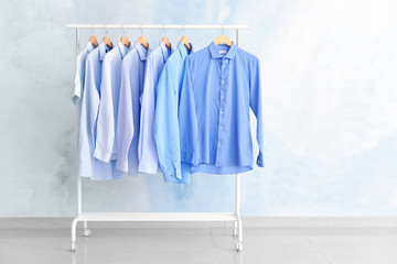 Rack with clothes after dry-cleaning near light wall