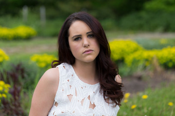 Horizontal closeup shot of pretty brunette young woman with dreamy expression in white lacy top against floral soft focus background