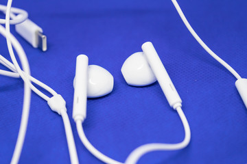 White earpods on blue background with the cable, music listening devices concept - Image