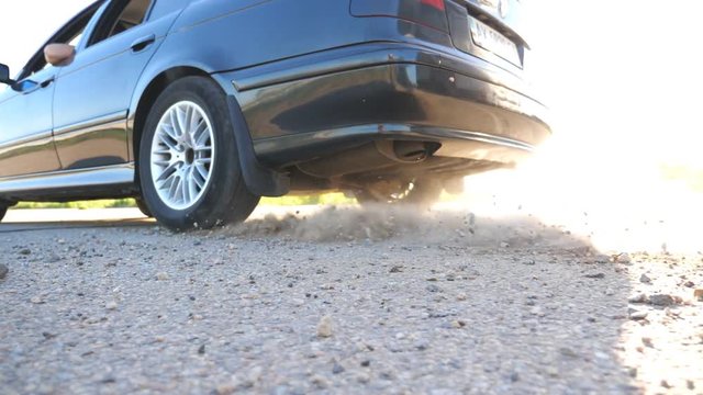 Wheel of car are slip on a asphalt road during start of movement. Small stones and dirt is fly out from under the tire of a auto. Vehicle quickly beginning motion. Concept of burnout. Slow motion