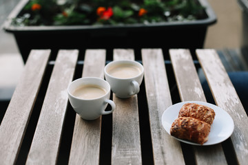 Coffee white cup, croissants on wooden table background. Breakfast concept. Freshly baked buns and coffee or cappuccino. Top view.