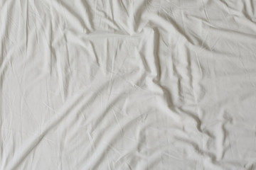 White fabric texture background. Wrinkled, crumpled fabric. Top view of unmade bed sheet after night sleep. Soft focus