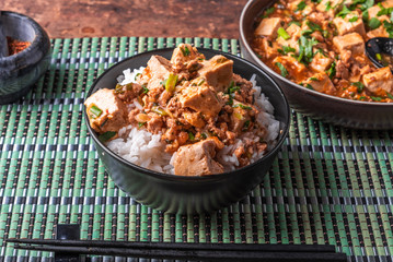 Traditional Chinese Sichuan cuisine - a bowl of rice with mapo tofu and a plate of mapo doufu on a bamboo napkin and a wooden rustic background