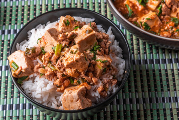 A popular Chinese Sichuan dish is a bowl of rice with spicy mapo tofu and a plate of mapo doufu on a bamboo napkin