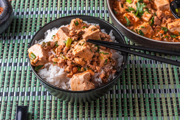 A popular Chinese Sichuan dish is a bowl of rice with spicy mapo tofu and a plate of mapo doufu on a bamboo napkin