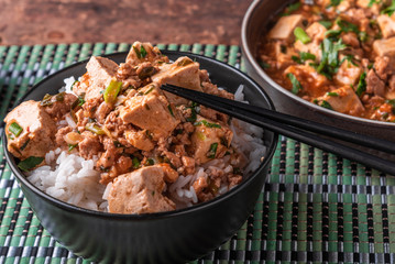 A popular Chinese Sichuan dish is a bowl of rice with spicy mapo tofu and a plate of mapo doufu on a bamboo napkin