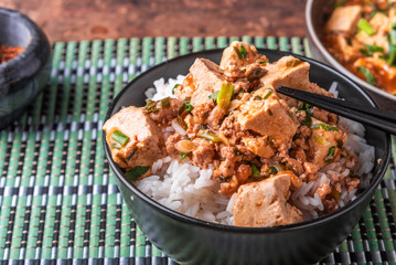 A popular Chinese Sichuan dish is a bowl of rice with spicy mapo tofu and a plate of mapo doufu on a bamboo napkin
