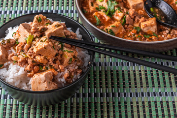 A popular Chinese Sichuan dish is a bowl of rice with spicy mapo tofu and a plate of mapo doufu on a bamboo napkin