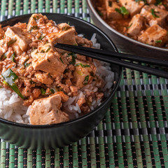 A popular Chinese Sichuan dish is a bowl of rice with spicy mapo tofu and a plate of mapo doufu on a bamboo napkin