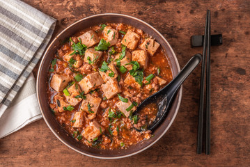 Popular Chinese Sichuan dish - a bowl of Mapo doufu on a rustic wooden table, top view - obrazy, fototapety, plakaty