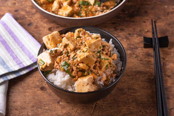 Popular Chinese Sichuan dish - a bowl of rice with spicy mapo tofu and a plate of mapo doufu on a rustic wooden table