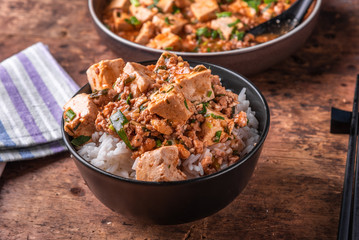 Popular Chinese Sichuan dish - a bowl of rice with spicy mapo tofu and a plate of mapo doufu on a rustic wooden table