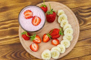 Glass of fresh smoothie of strawberry and banana on a wooden table. Top view