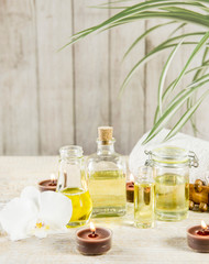 Different size and shape transparent glass jars and bottles with massage and essential oils on table, natural wooden background, white orchid and candles for decoration. Beauty spa background concept.